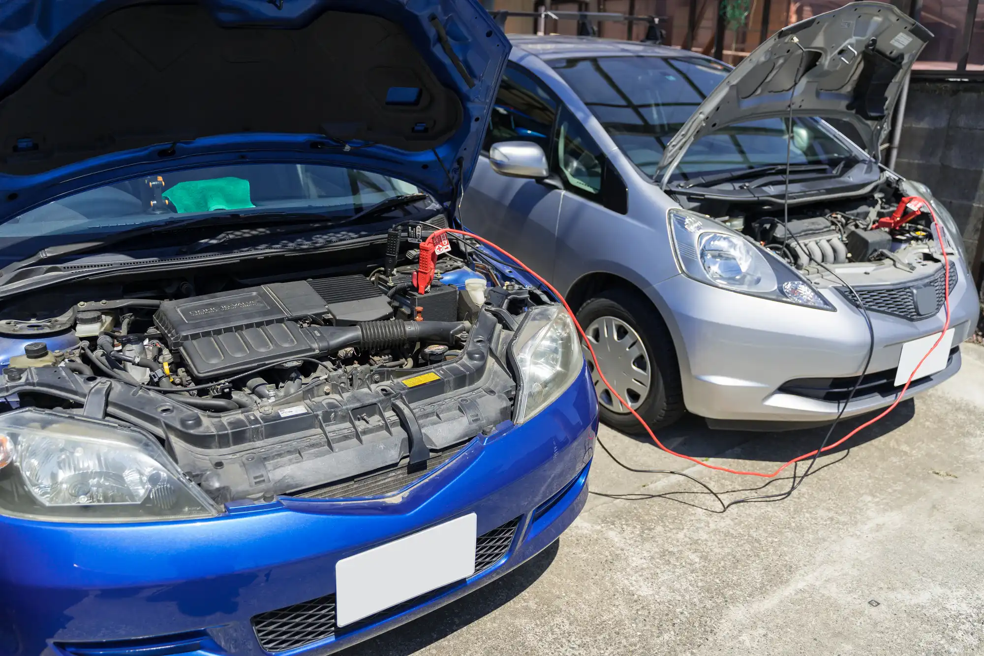 青とシルバーの車のバッテリーをブースターケーブルで繋いでいる