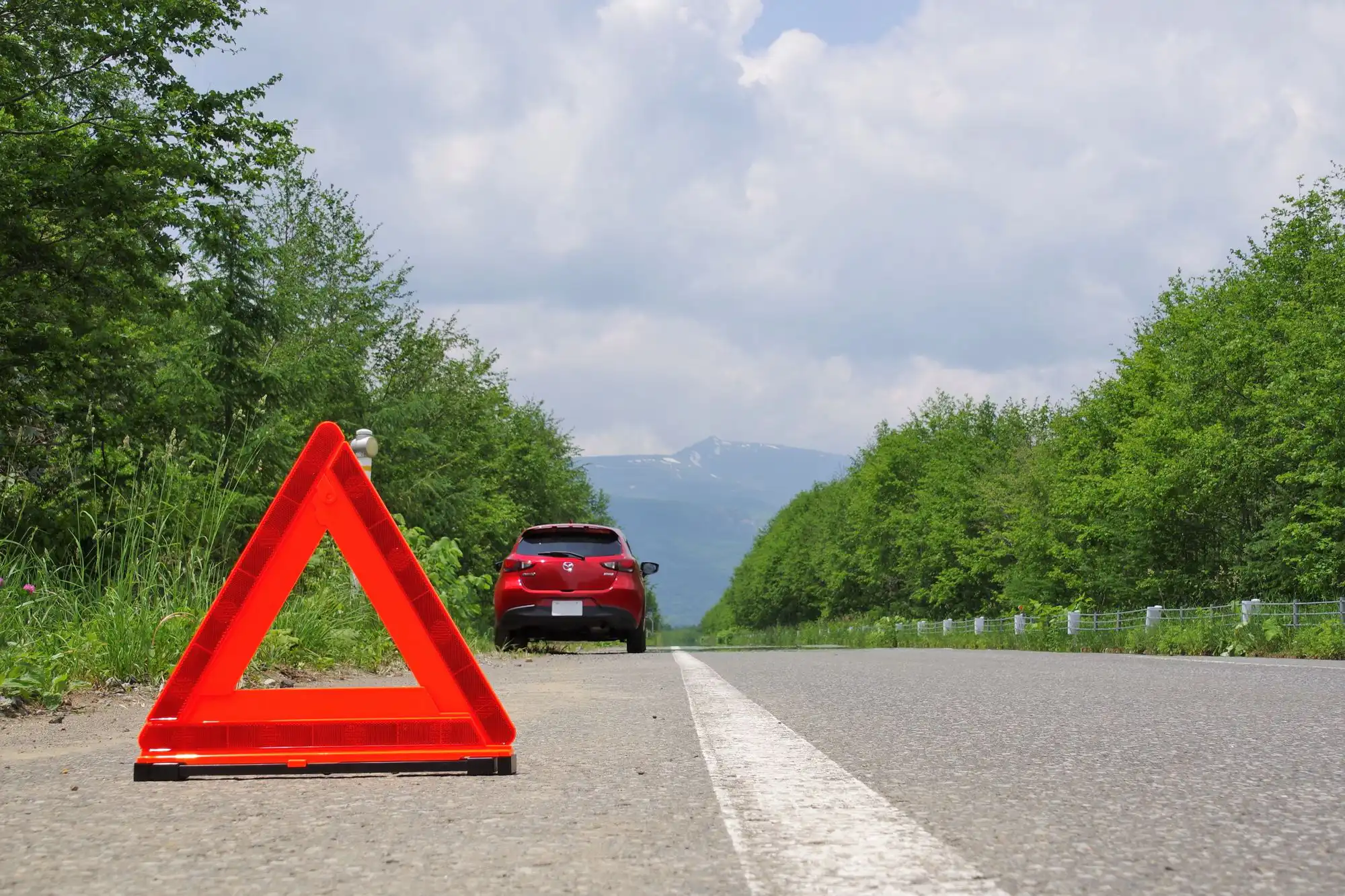 三角表示板を置いた先に赤い車が止まっている