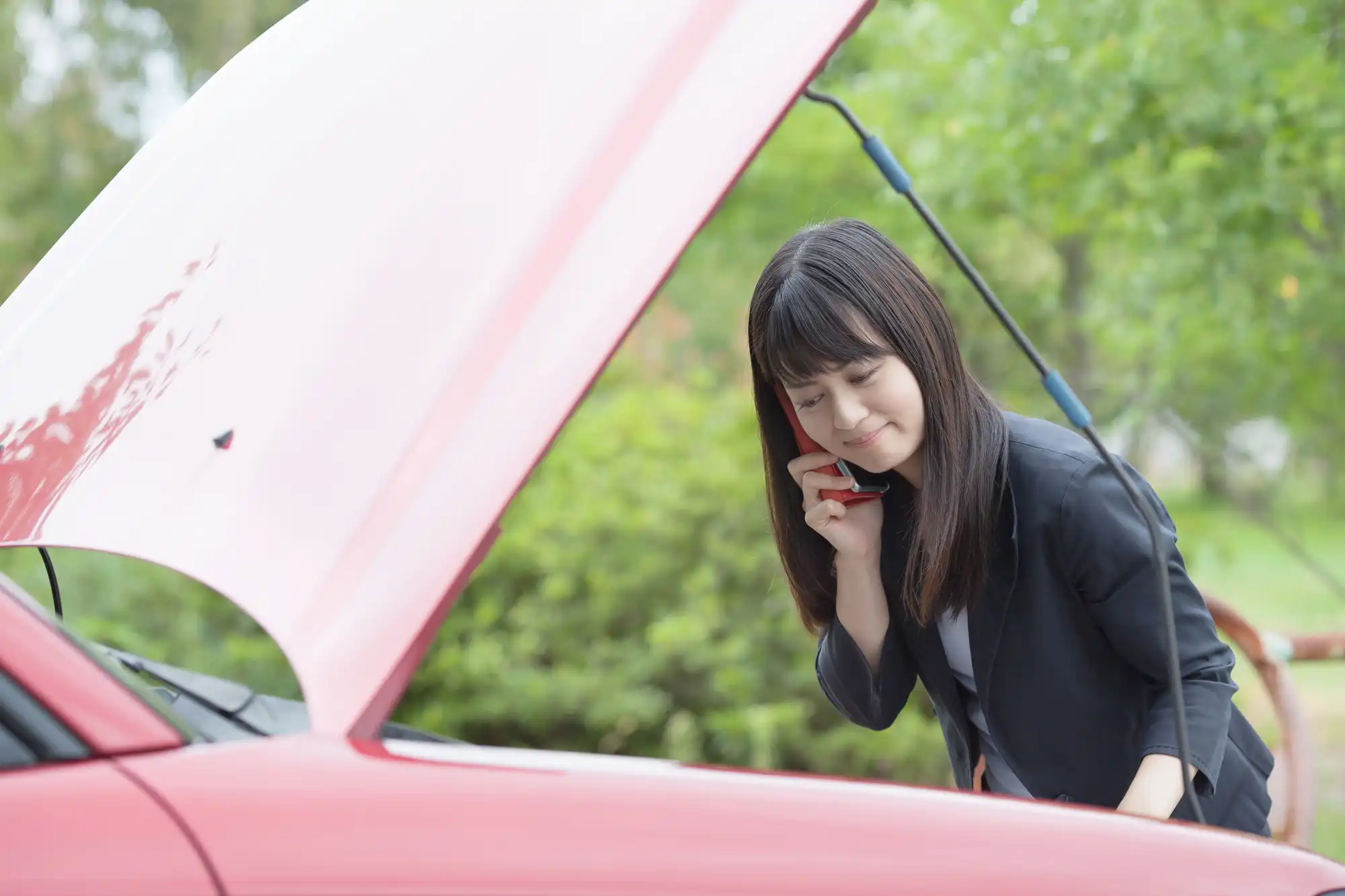 車のボンネットを開けて中を見ながら、電話している女性