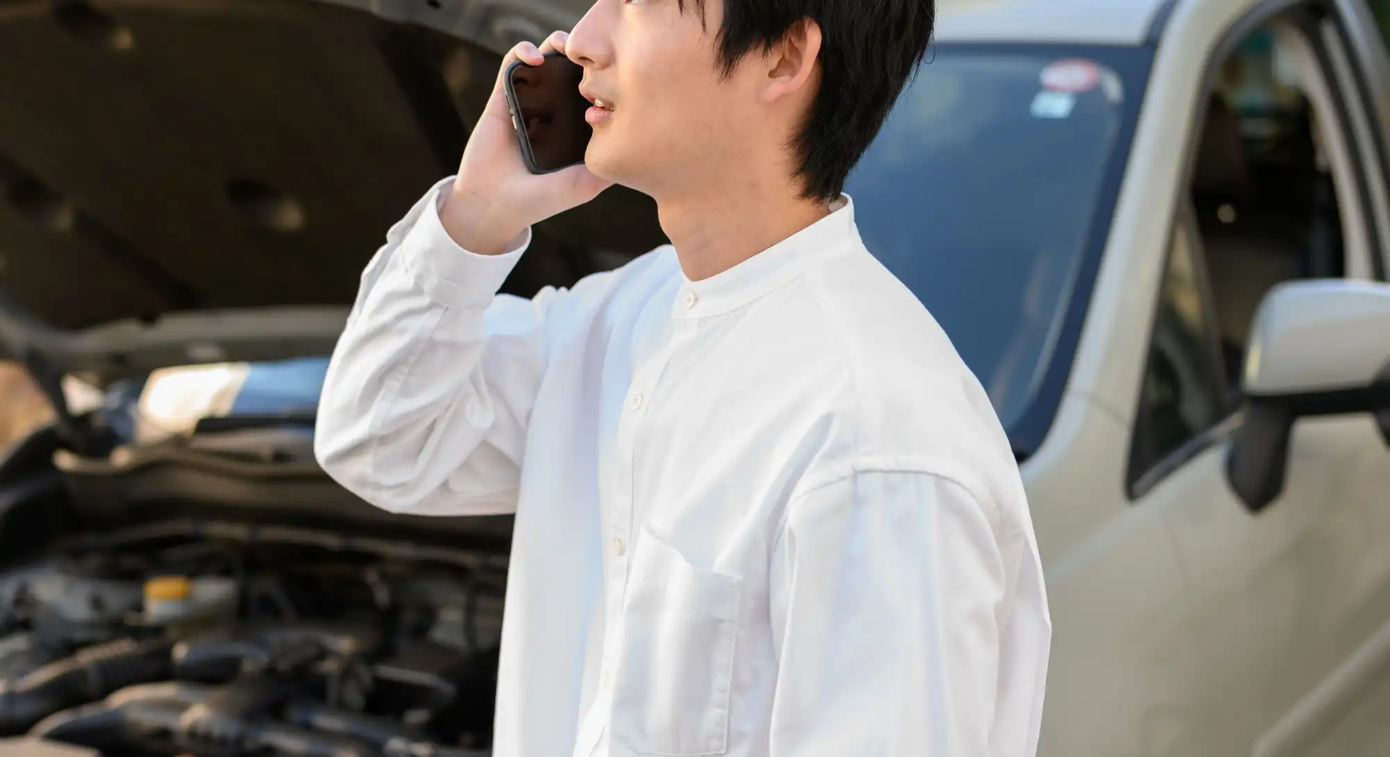 ボンネットを開けた白い車の前で電話する男性