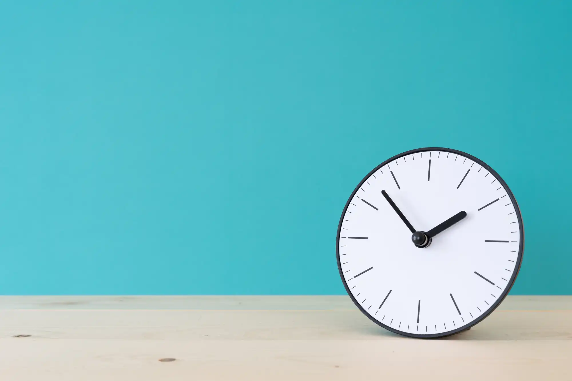 ブルーグリーンの壁の前にある机に置かれた時計
