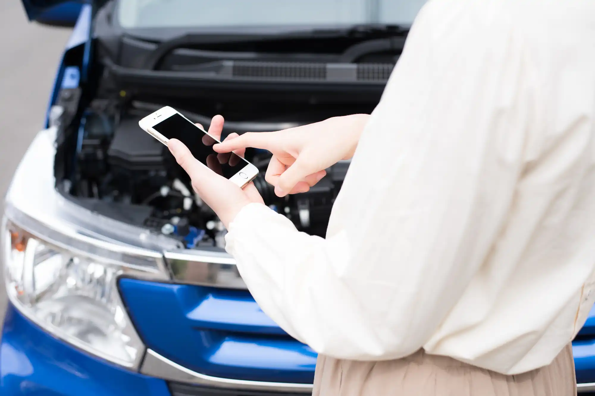ボンネットを開けた青い車の前で電話する人
