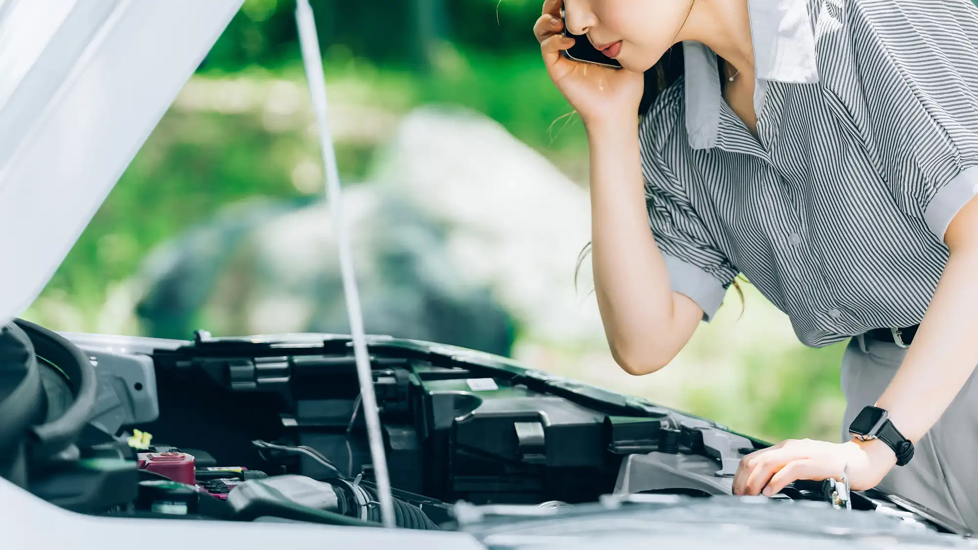 車のエンジンルームを見ながら電話する女性