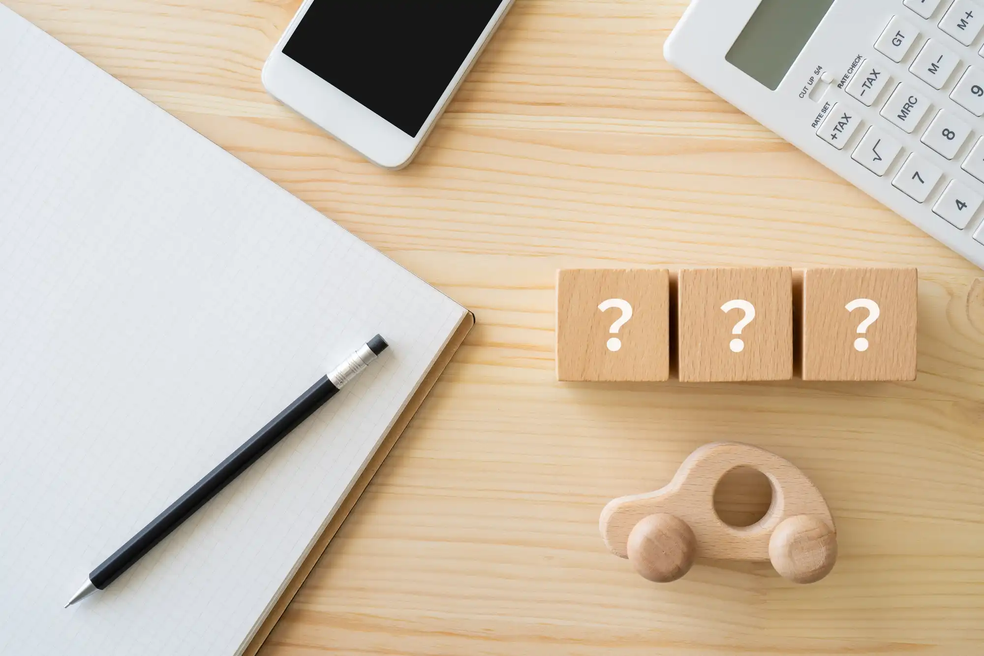 机の上に置かれた?のキューブが3個とノート、シャーペン、電卓、スマホ